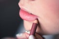 Woman putting on makeup, painting lips with red lipliner. Closeup of lips touched with pencil, studio. Royalty Free Stock Photo