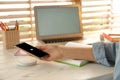 Woman putting mobile phone onto wireless charger at white wooden table, closeup. Modern workplace accessory