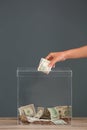 Woman putting money into donation box on table against background Royalty Free Stock Photo