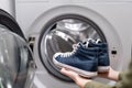 Woman putting pair of blue sneakers into washing machine, close up. Royalty Free Stock Photo