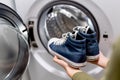 Woman putting pair of blue sneakers into washing machine, close up. Royalty Free Stock Photo