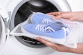 Woman putting pair of sport shoes in mesh laundry bag into washing machine, closeup