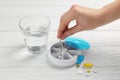 Woman putting pill into plastic box at white wooden table, closeup Royalty Free Stock Photo