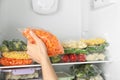 Woman putting plastic bag with carrot in refrigerator with frozen vegetables