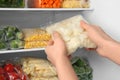 Woman putting plastic bag with cauliflower in refrigerator with frozen vegetables Royalty Free Stock Photo