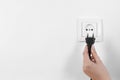 Woman putting plug into power socket on white, closeup. Electrician`s equipment