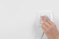 Woman putting plug into power socket on white, closeup. Electrician`s equipment