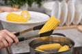 Woman putting raw corn cob into stewpot Royalty Free Stock Photo