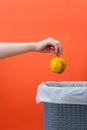 Woman putting the rotten apple in waste bin on an orange background