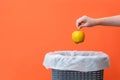 Woman putting the rotten apple in waste bin on an orange background