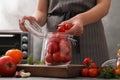 Woman putting tomatoes into glass jar at kitchen table. Pickling vegetables