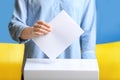 Woman putting voting paper into ballot box against Ukrainian flag Royalty Free Stock Photo