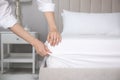 Woman putting white fitted sheet over mattress on bed indoors, closeup