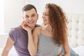 Woman in pyjamas sits with her husband early in morning, sits on bed, touches him gently with hand. Pretty curly female spend time