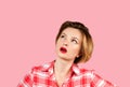 Woman with questioning expression looking up on pink background