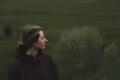 Woman in a rain anorak stands on the hill, deep green background.