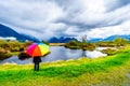 Woman with a rainbow colored Umbrella under dark rain clouds on a cold spring day at the lagoons of Pitt-Addington Marsh Royalty Free Stock Photo