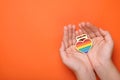 Woman with rainbow heart shaped pendant on orange background, top view and space for text. LGBT pride