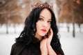 woman in a raincoat with a fur hood and a crown on her head against the background of a winter forest Royalty Free Stock Photo