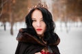 woman in a raincoat with a fur hood and a crown on her head against the background of a winter forest Royalty Free Stock Photo