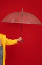 Woman in raincoat holding transparent umbrella against red backgroud, studio shot, crop. Autumn accessories concept Royalty Free Stock Photo