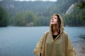 Woman in raincoat near lake in rainy day.