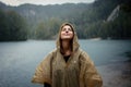 Woman in raincoat near lake in rainy day.