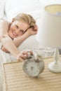 Woman Reaching For Alarm Clock While Lying On Bed