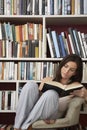 Woman Reading Against Bookshelves At Home
