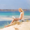 Woman reading book, enjoying sun on beach. Royalty Free Stock Photo