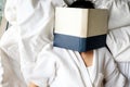 Woman reading a book with the face covered by the book