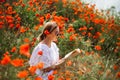 Woman reading a book in a field of red poppies in spring flowers mood.