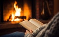 Woman reading a book by the fireplace in a cozy warm home close up, autumn vibe concept