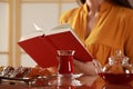 Woman reading book, glass of traditional Turkish tea and snacks on table indoors, selective focus Royalty Free Stock Photo