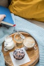 Woman reading book and having blueberry muffin with coffee, sugar and milk on wooden tray and comfy sofa with blue wool knit Royalty Free Stock Photo