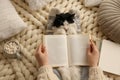 Woman reading book and holding adorable cat on knitted blanket, top view Royalty Free Stock Photo