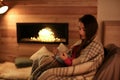 Woman reading book near decorative fireplace at home.
