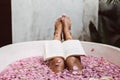 Woman reading book while relaxing in bath tub with flower petals Royalty Free Stock Photo