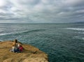 Woman reading a book on a seaside cliff looking out onto the Pacific Ocean