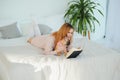 A woman reading a book and smiling as she sits in bed. The alarm clock on the desk beside her Royalty Free Stock Photo