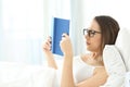 Woman reading a book wearing eyeglasses on the bed Royalty Free Stock Photo