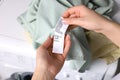 Woman reading clothing label with care symbols and material content on green shirt near washing machine, closeup