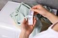 Woman reading clothing label with care symbols and material content on green shirt near washing machine, closeup