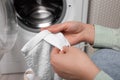 Woman reading clothing label with care symbols and material content on white towel near washing machine, closeup