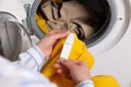 Woman reading clothing label with care symbols and material content on yellow shirt near washing machine, closeup