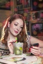 Woman reading a message on her mobile phone and drinking a mojito long drink with lime