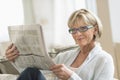 Woman Reading Newspaper While Relaxing On Sofa Royalty Free Stock Photo