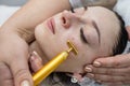 woman receive pulse face massaging at spa, vibrating golden facial massager on female face