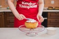 A woman in a red apron decorates a cupcake with white cream.
