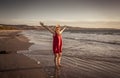 Woman in red with arms outstretched by the sea at sunrise enjoying freedom and outdoors life Royalty Free Stock Photo